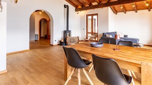 Un vaste espace de vie doté d’un plafond en bois, d’une cheminée, d’un canapé et d’une table à manger avec des chaises.
