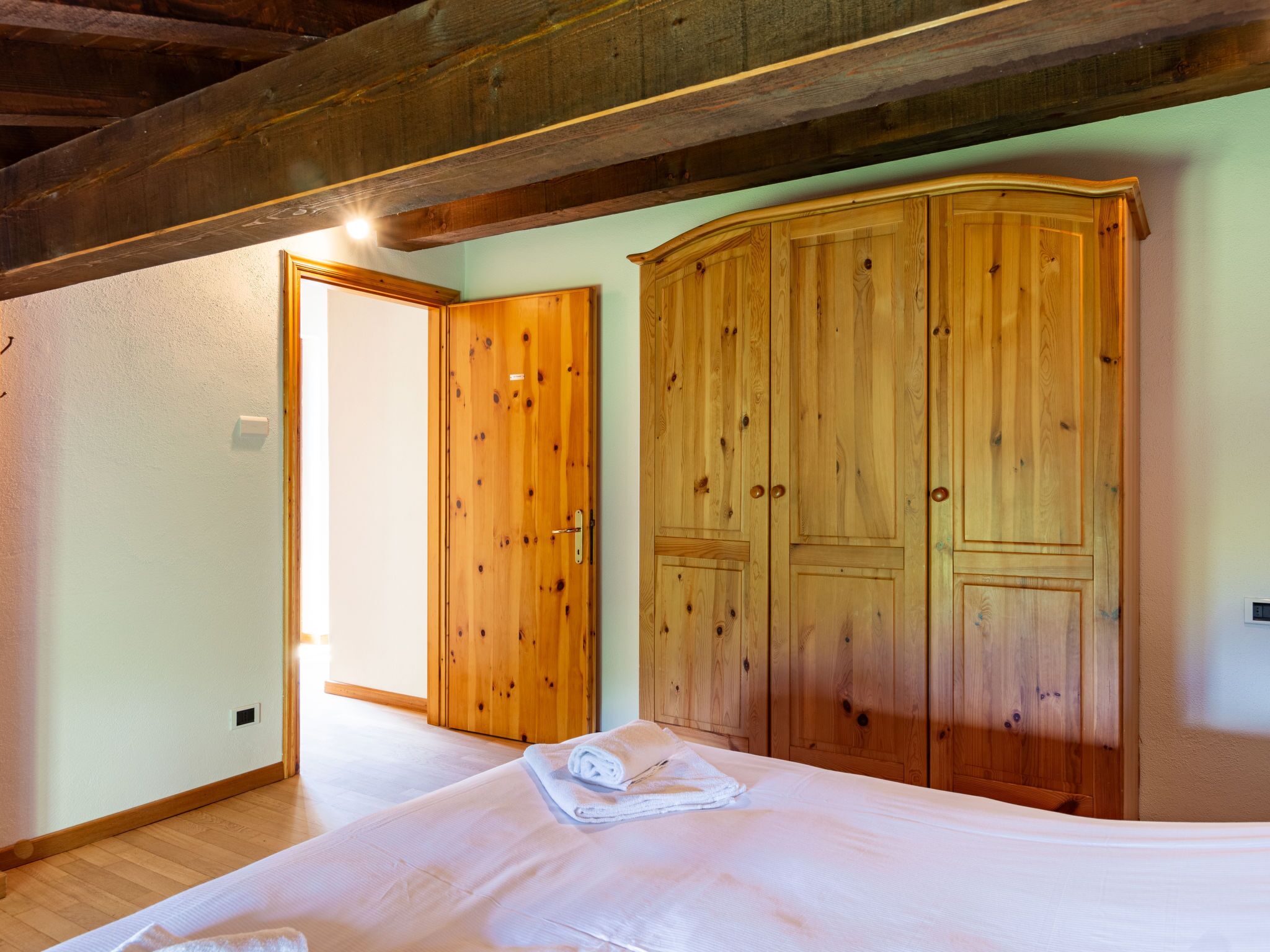 A bedroom with a wooden wardrobe, a bed with a white duvet, and a wooden ceiling.