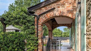 Un espace extérieur aménagé en patio, avec une arche en briques, une table et des chaises, et une vue sur la végétation environnante.