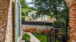 Un chemin de pierres mène à un petit jardin, délimité par un mur de pierres et une clôture en métal.