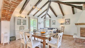 Un coin repas avec une table en bois et des chaises blanches, une cuisine avec des meubles blancs et une cheminée en briques.