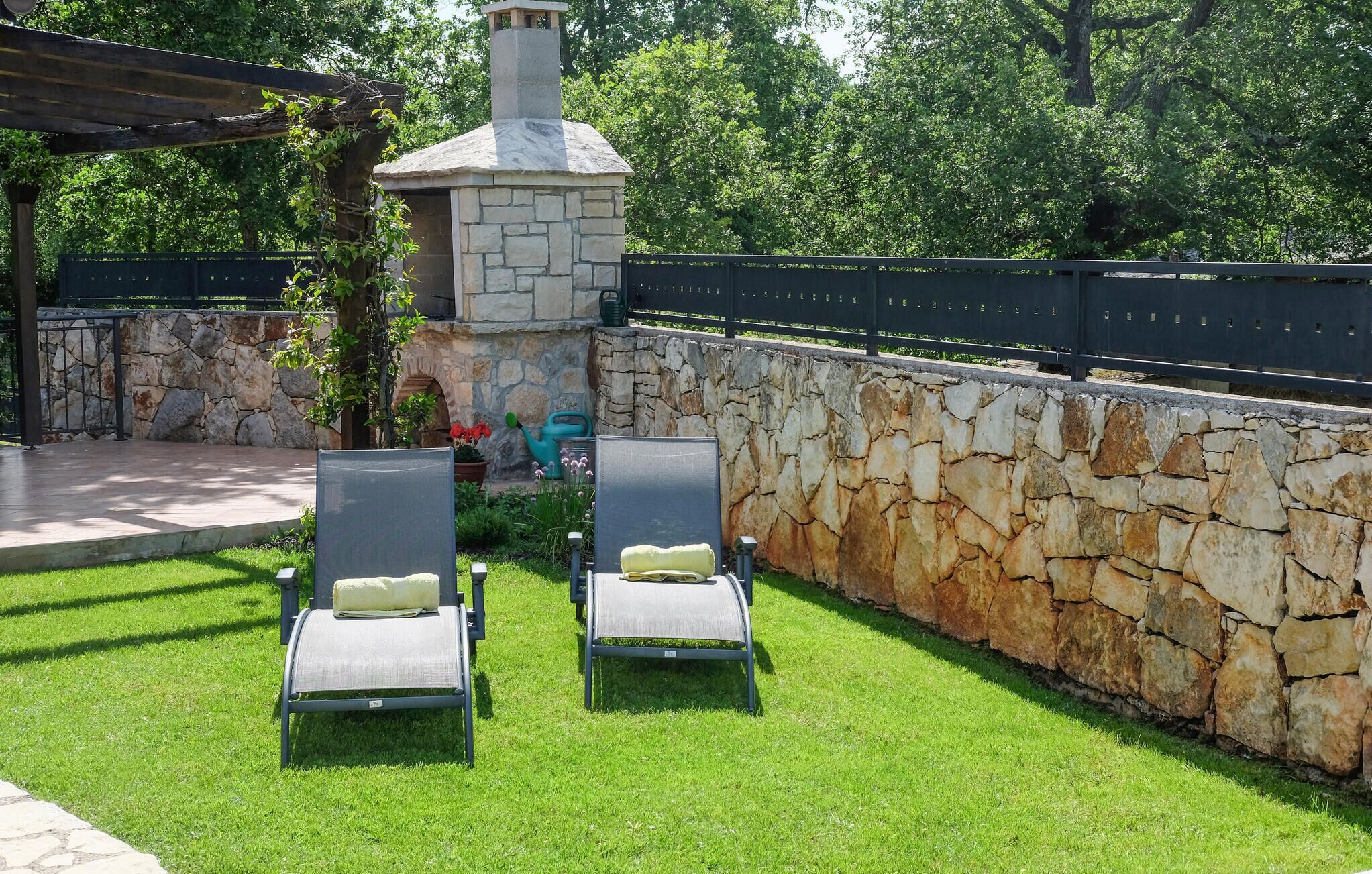 A stone-built outdoor seating area with two lounge chairs and a stone chimney.