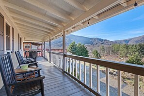 A wooden deck with a table and chairs, overlooking a mountainous landscape. - Smoky Mountain Solace-Stunning Views! Pet Friendly (Maggie valley)