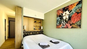 Ein Hotelzimmer mit Bett, Schrank, einem Gemälde und einer Tür zu einem anderen Raum.