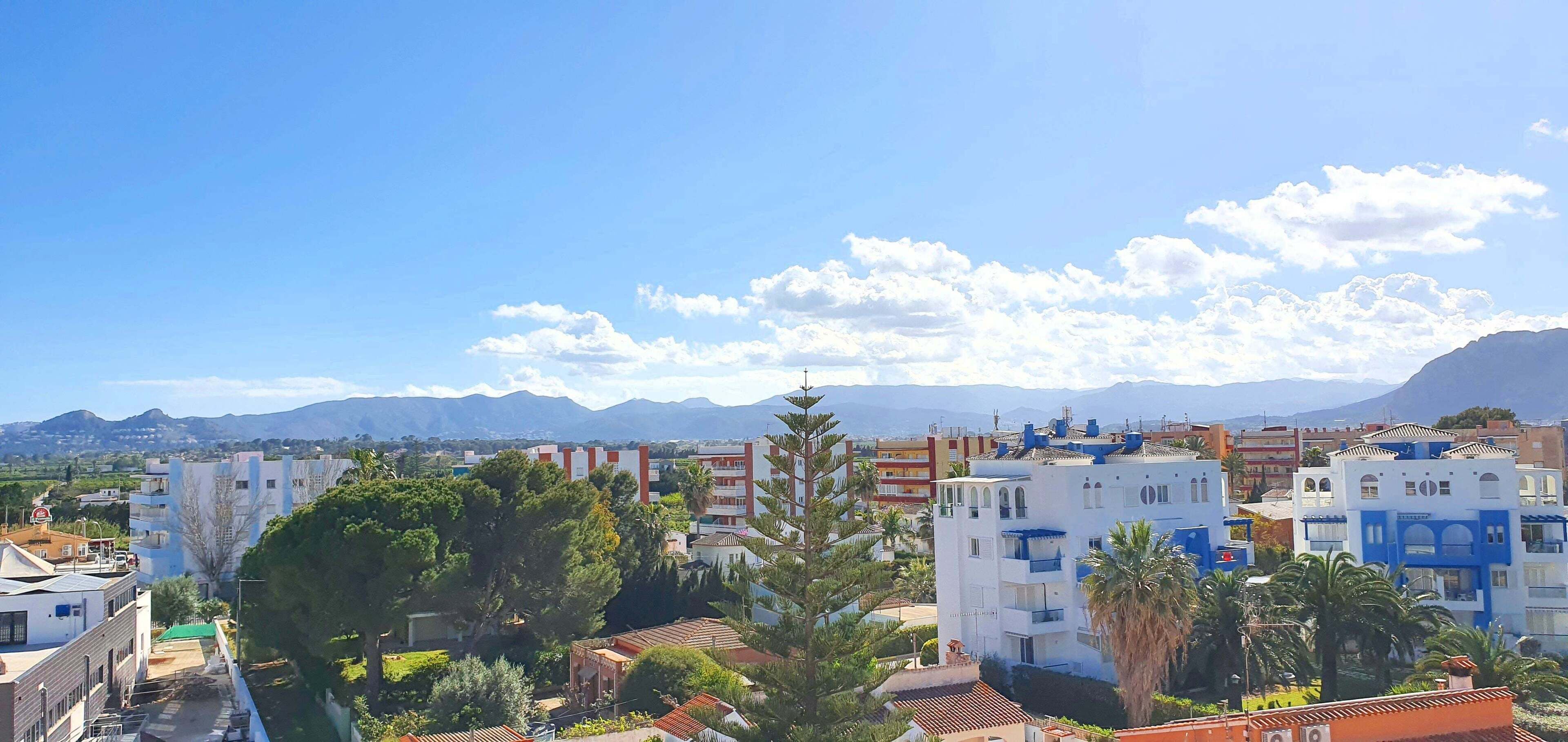 Un barrio residencial con edificios, árboles y montañas al fondo.