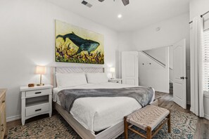 Een slaapkamer met een bed, nachtkastjes, een bankje, een schilderij en een deur.