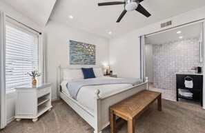Un dormitorio con cama, mesita de noche, banco y ventilador de techo.