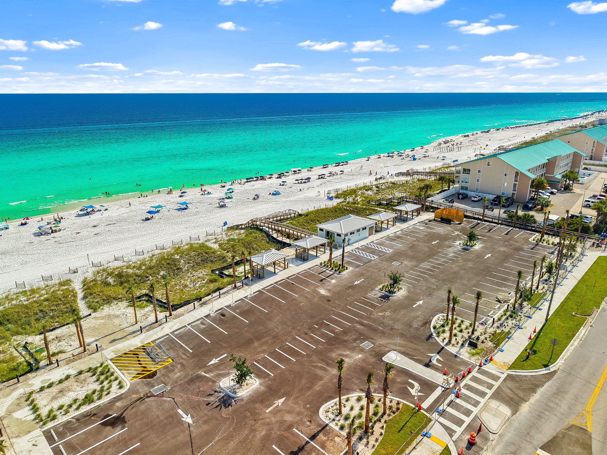 An aerial view of a beachside hotel with a parking lot, beach, and ocean.