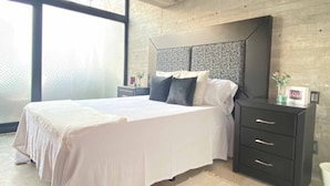 Une chambre à coucher moderne avec un grand lit, une tête de lit sombre et une table de chevet dotée de tiroirs.