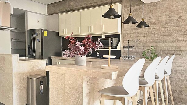 Une cuisine moderne dotée d’un îlot central, d’appareils électroménagers en acier inoxydable et de luminaires suspendus.