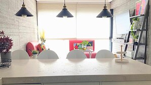 Une cuisine avec un plan de travail blanc, trois suspensions, une chaise rouge et une table à manger avec des chaises.