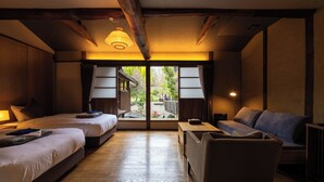 Habitación de hotel con dos camas, un sofá, una mesita y vistas a un jardín a través de un ventanal corredero.