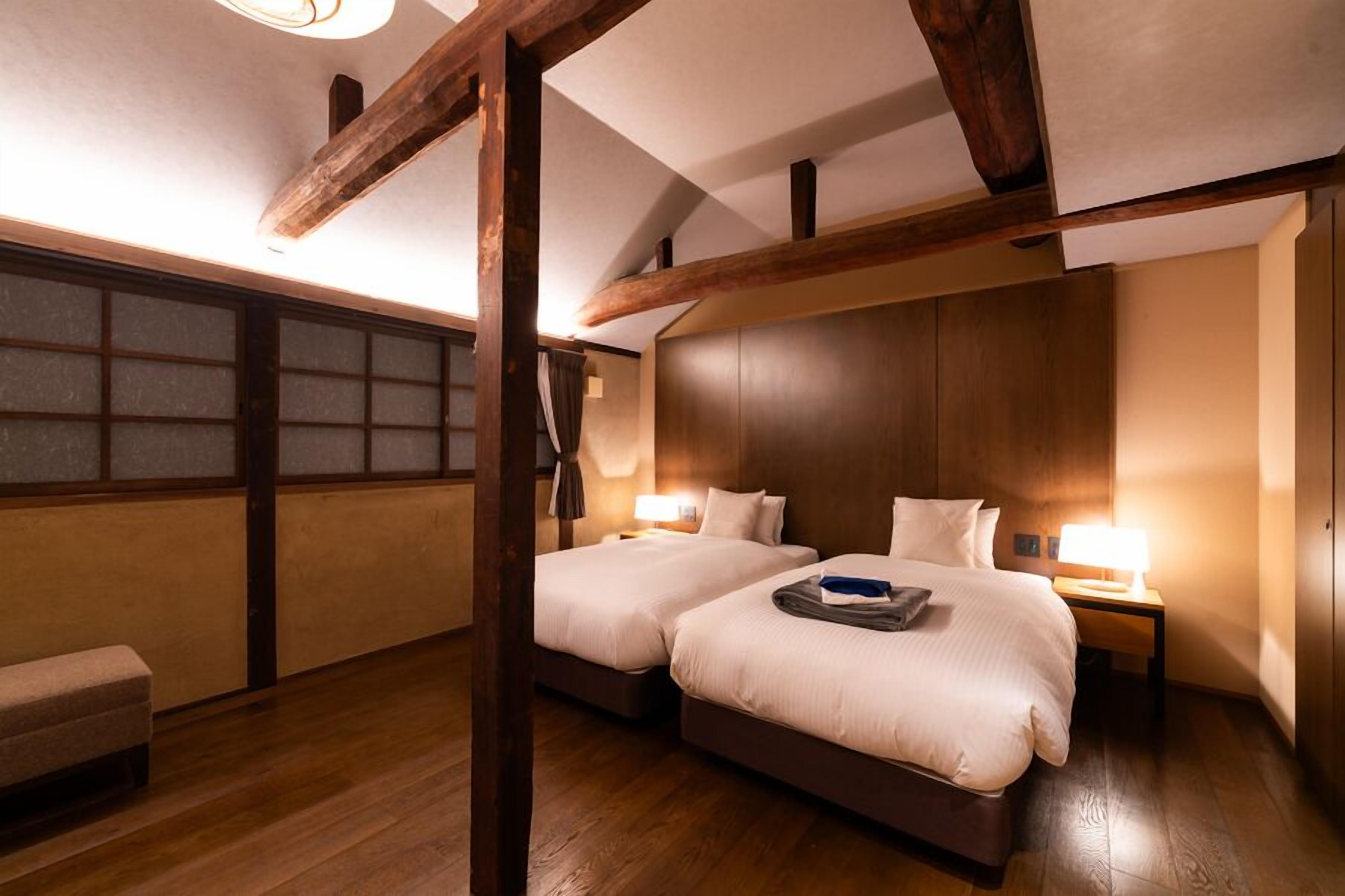 A hotel room with two beds, wooden beams, a bench, and a view through a window.