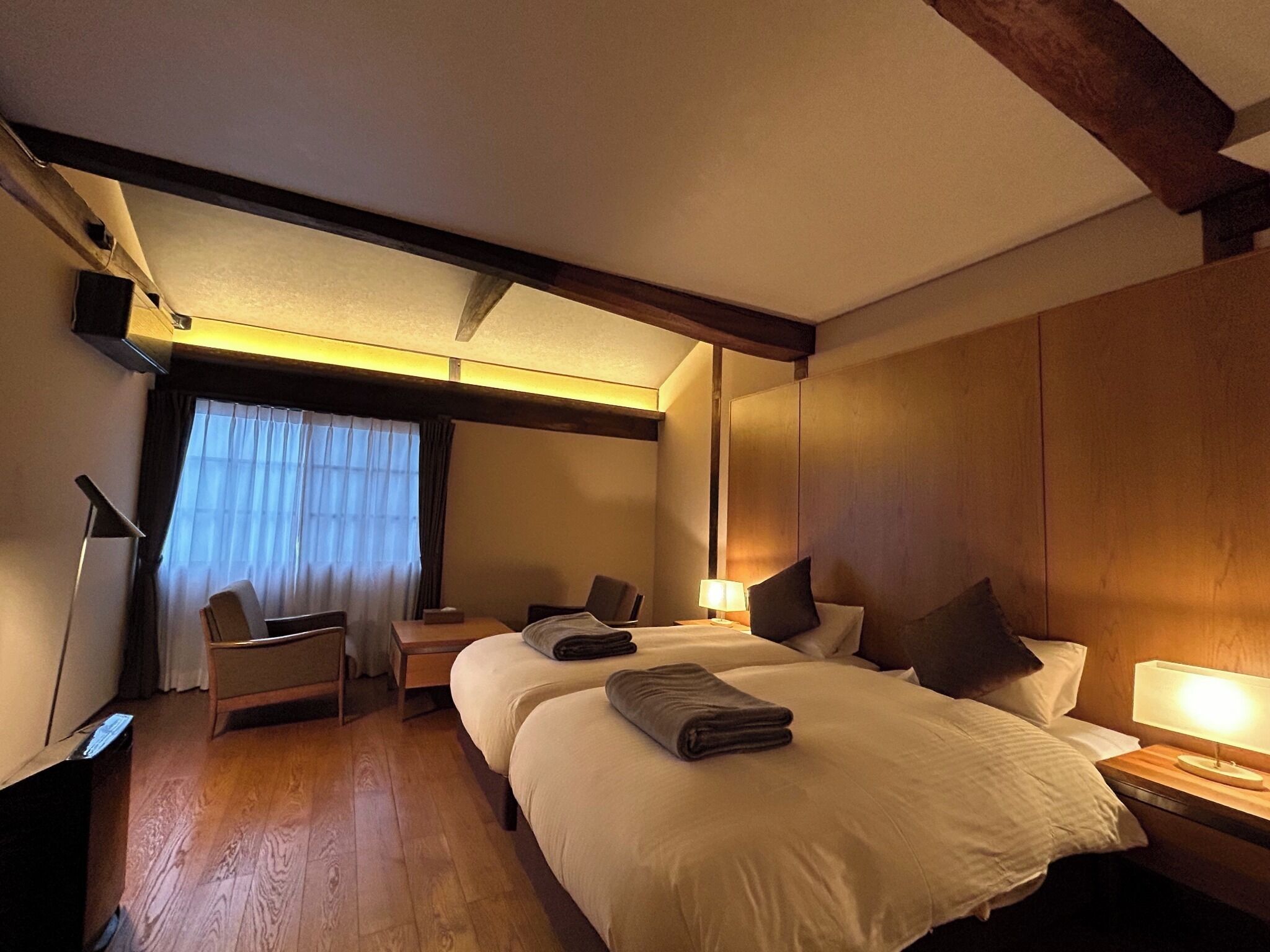 A hotel room with two beds, a desk, a chair, and a window with curtains.