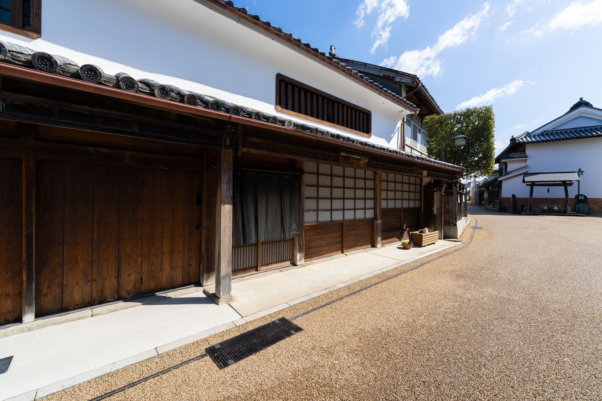 A traditional Japanese building with wooden sliding doors, a tiled roof, and a gravel street.