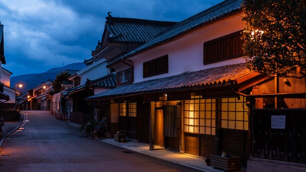 Una calle japonesa tradicional al anochecer, con edificios de tejados alicatados y fachadas de madera.