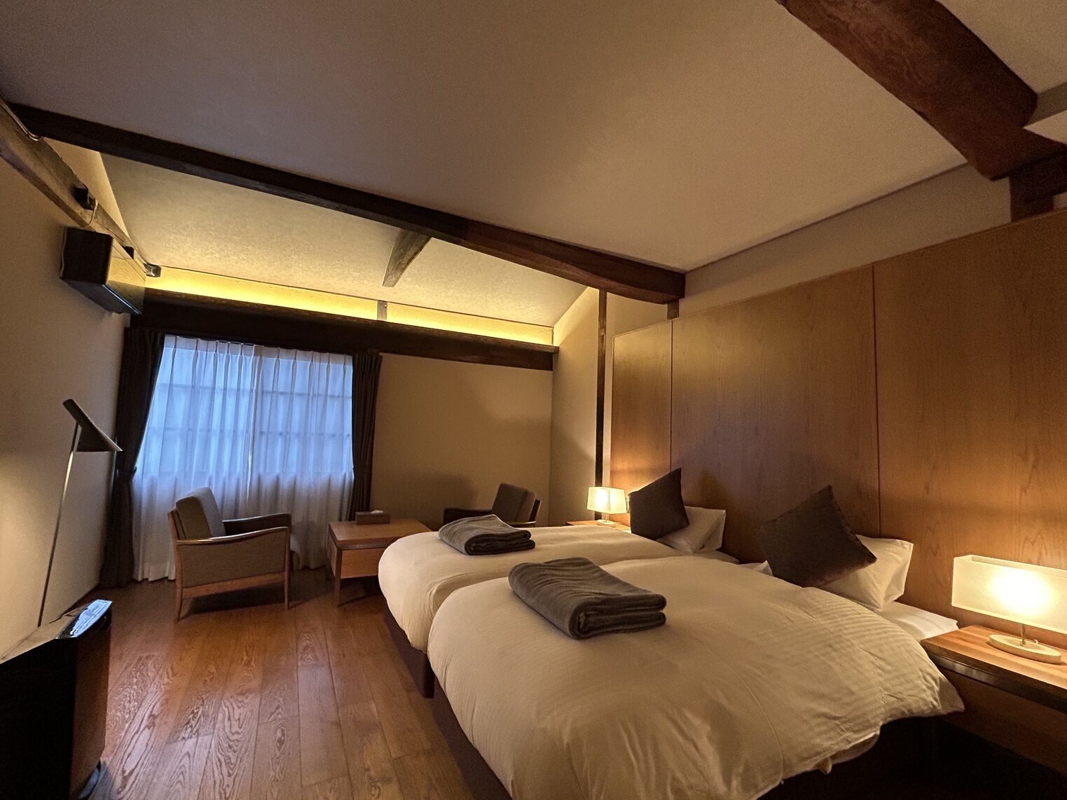 A hotel room with two beds, a desk, a chair, and a window with curtains.