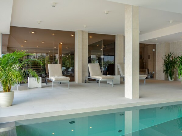 Un espace piscine intérieur moderne, doté de chaises longues et de plantes en pot.