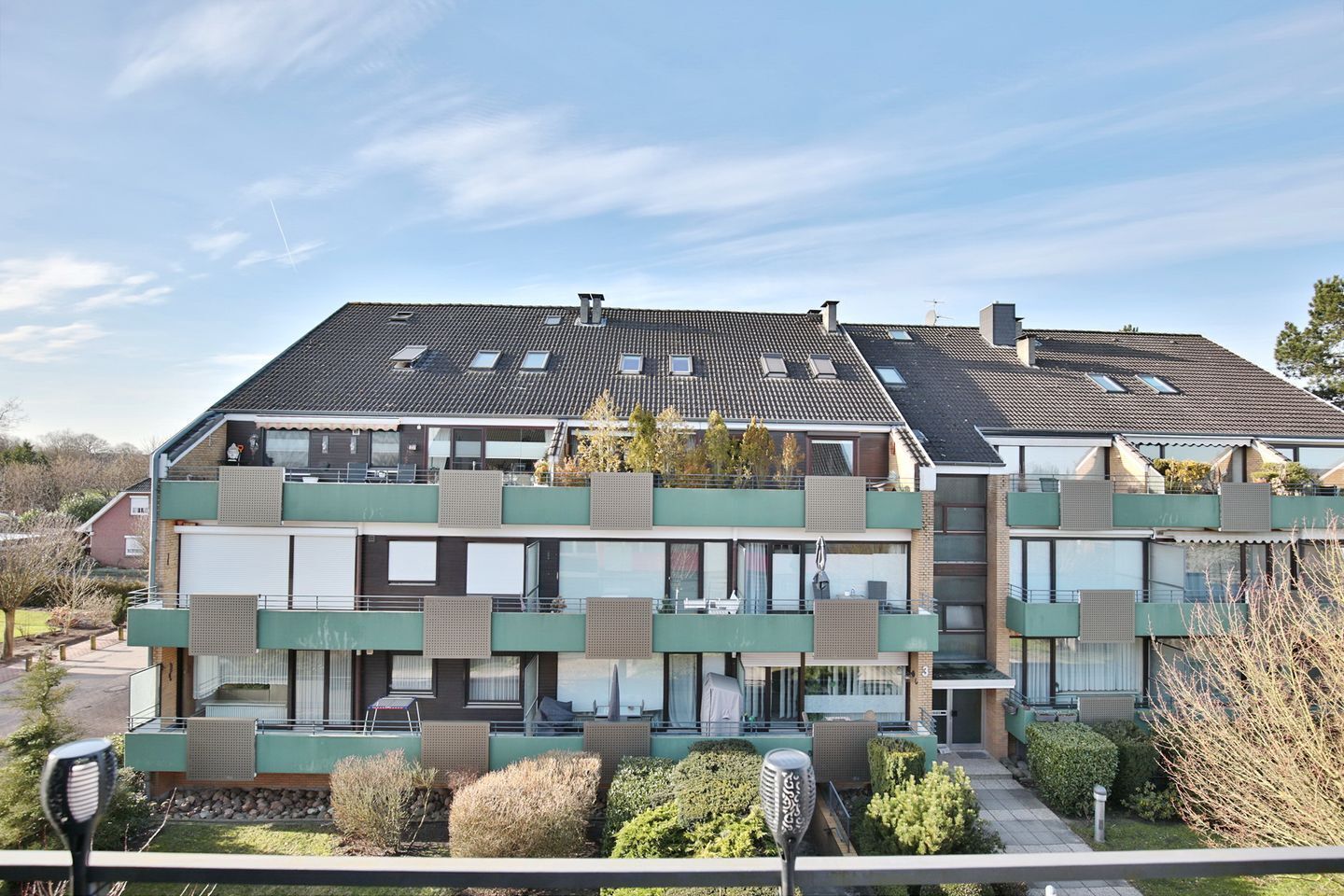 A modern multi-story residential building with balconies, large windows, and a flat roof with skylights.
