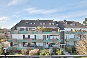En modern flervåningsbyggnad med bostäder, balkonger, stora fönster och ett platt tak med takfönster.