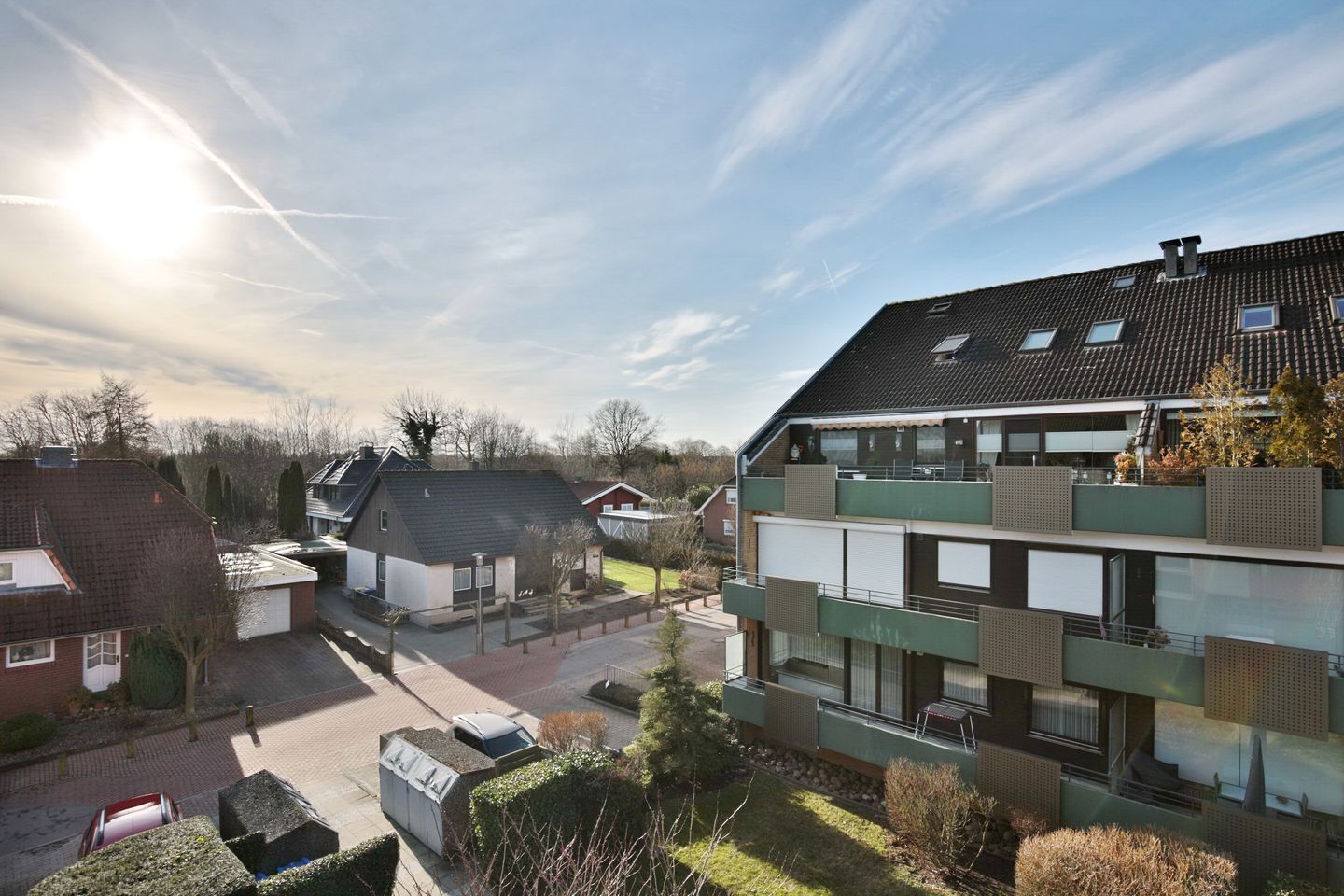 En modern bostadsbyggnad med flera balkonger, en parkeringsplats och en klar himmel.