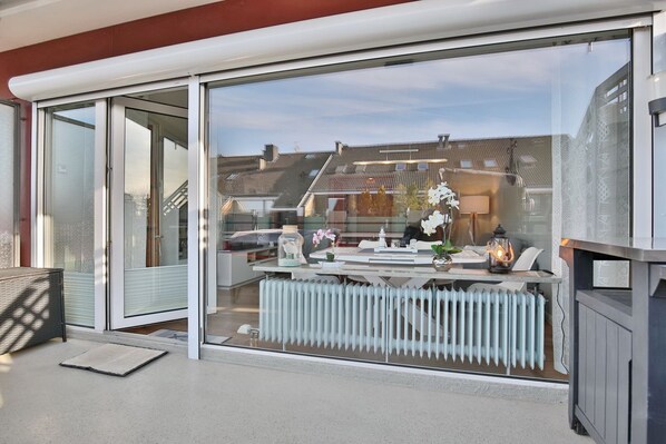 A modern living room with a glass sliding door, a white radiator, and a dining area with a table and chairs.