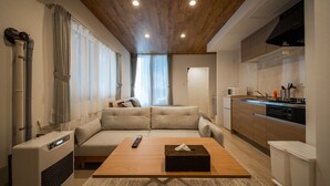 Um espaço de estar moderno com sofá, mesa de centro de madeira, cozinha equipada com micro-ondas e um ar condicionado visível.