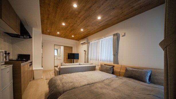 Quarto com duas camas, teto de madeira e cozinha compacta.