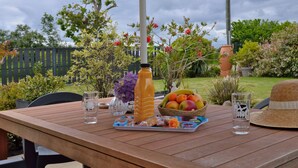 Une table à manger extérieure avec un panier de fruits, une bouteille et des verres.