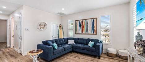 Uma sala de estar moderna com um sofá modular, piso de madeira e uma pintura com tema praiano.