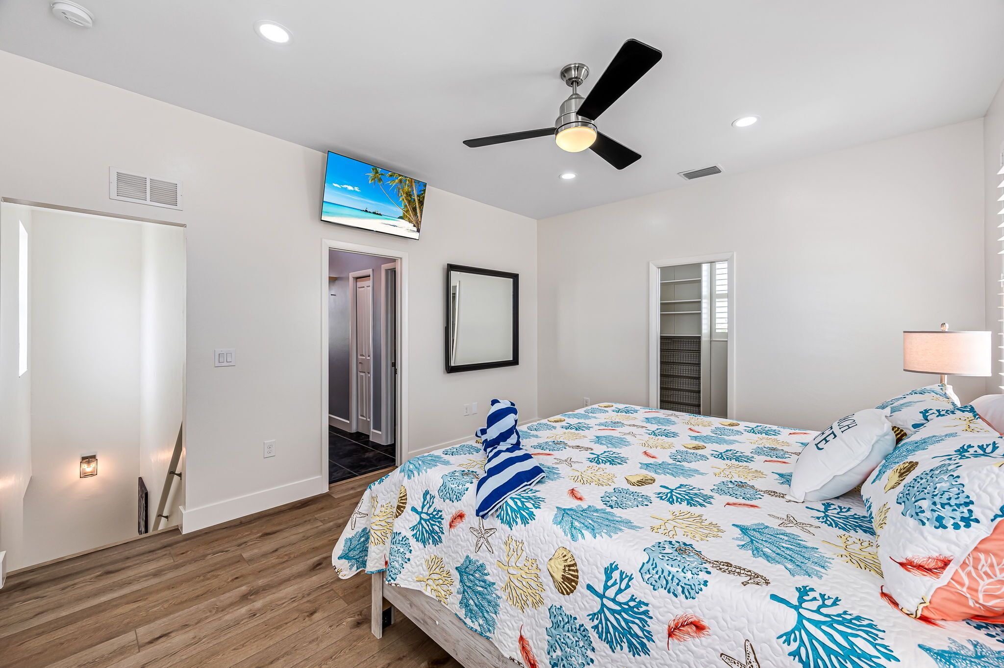 A bedroom with a bed, ceiling fan, and a TV mounted on the wall.