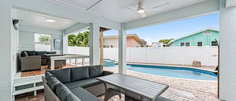 A covered patio area with a pool, outdoor furniture, and a view of neighboring houses.