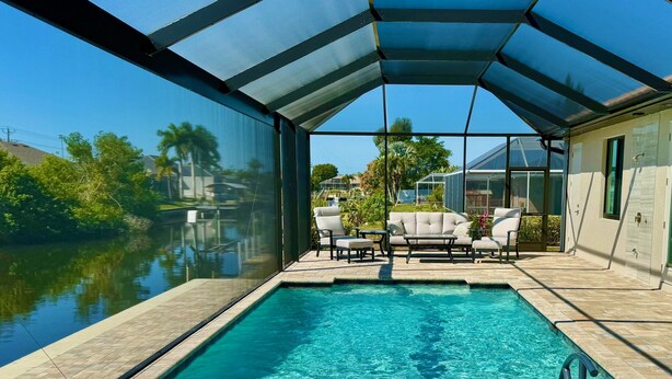 A swimming pool with a covered patio area, outdoor furniture, and a view of a residential neighborhood.