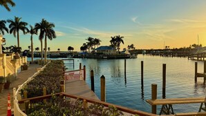 A waterfront promenade with a wooden deck, palm trees, and a marina with boats.