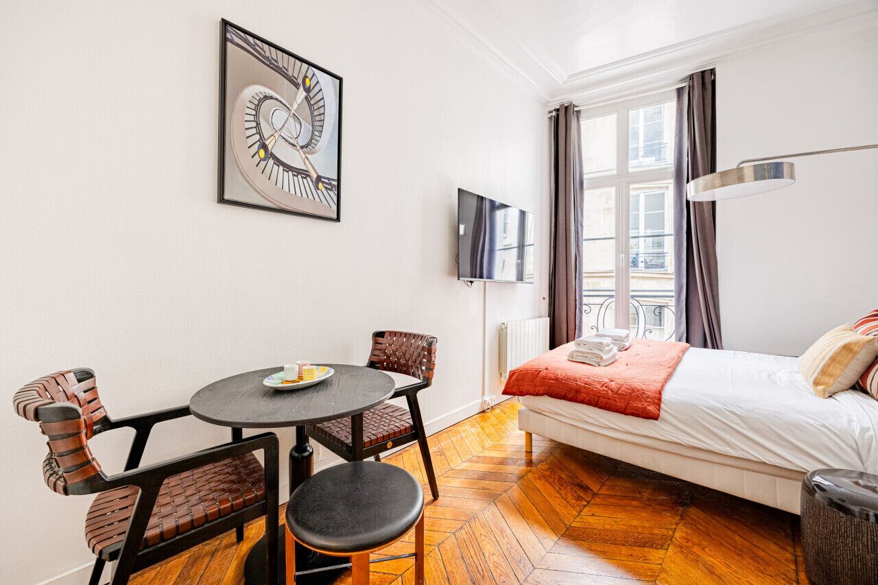 A hotel room with a bed, a round table with chairs, a TV, and a window with curtains.