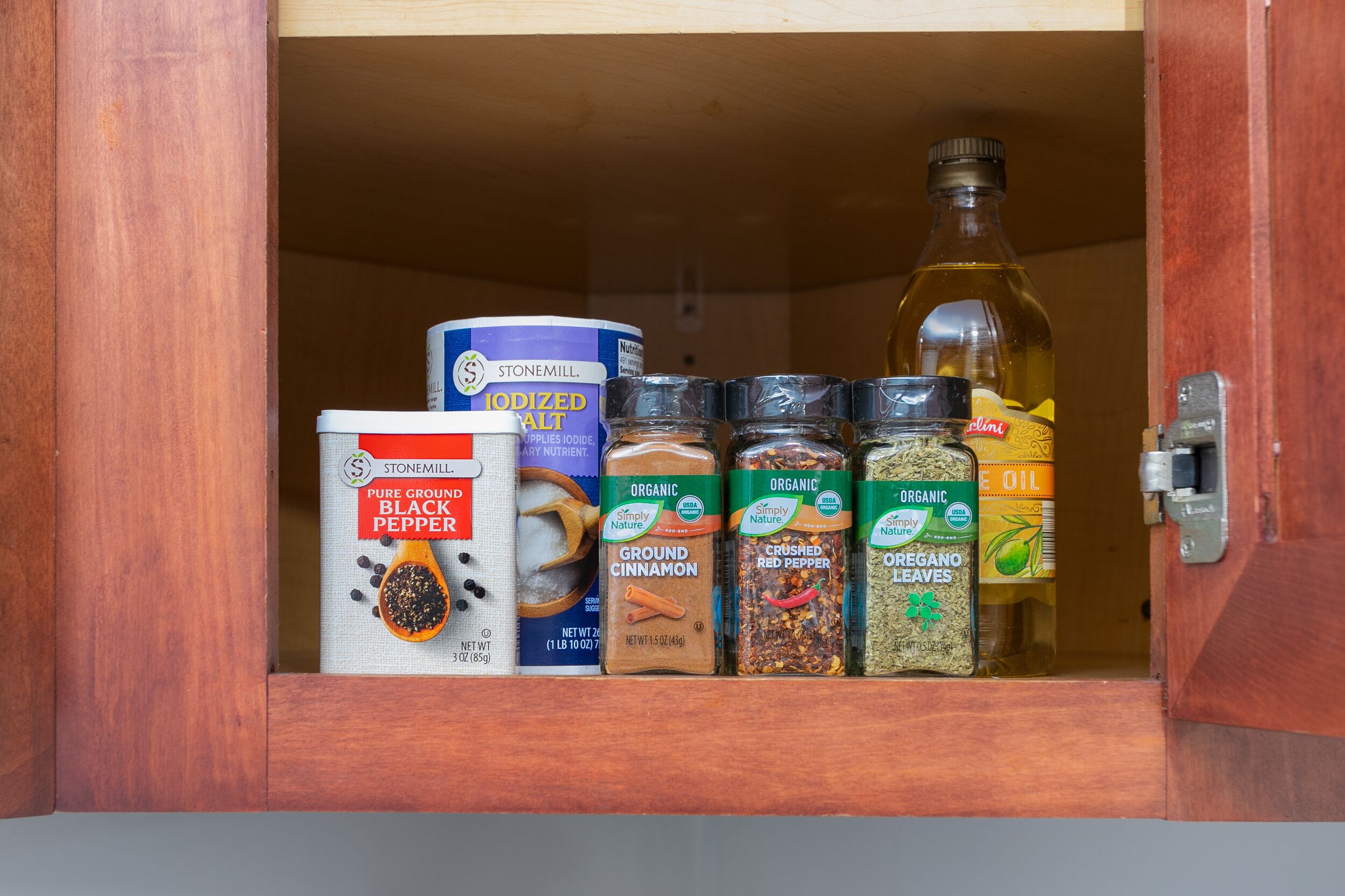A wooden cabinet with various spice containers and a bottle of oil.