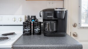 Una encimera de cocina con una cafetera Keurig, dos recipientes etiquetados 'Premium Sugar' y 'Premium Coffee Products', y una jarra de café.