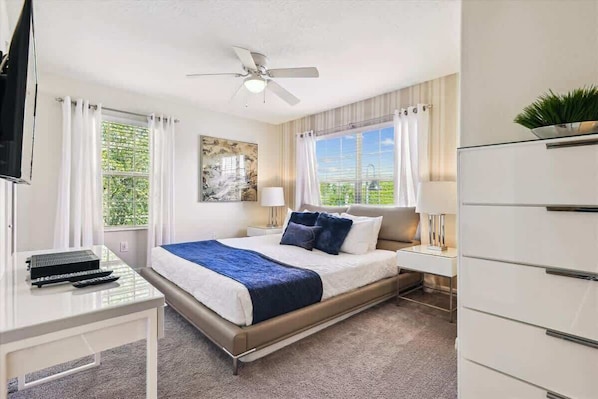 Habitación de hotel con una cama, un escritorio con computadora, un ventilador de techo y una ventana con cortinas.