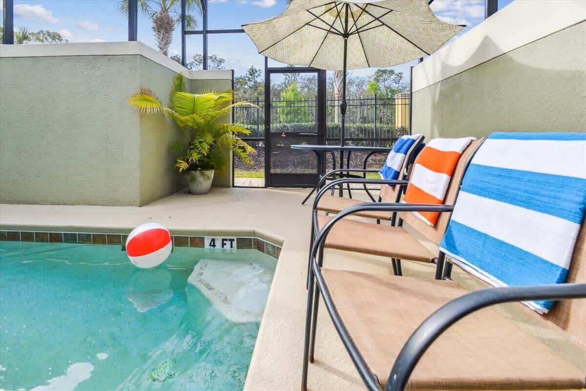 A pool area with lounge chairs, a beach ball, and a potted plant.