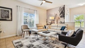 A living room with a sofa, armchairs, a coffee table, a ceiling fan, and a large wall mural. - 5BD Paradise Palms Resort Near Parks (PP 8976) (Kissimmee)