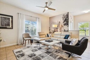 Una sala de estar con sofá, sillones, una mesa de centro, un ventilador de techo y un mural grande en la pared.