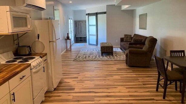 A modern kitchen with white appliances, a dining area with a wooden table and chairs, and a living room with a sofa and a patterned rug. - Cozy Apartment located on our 5-acre property (Winchester)