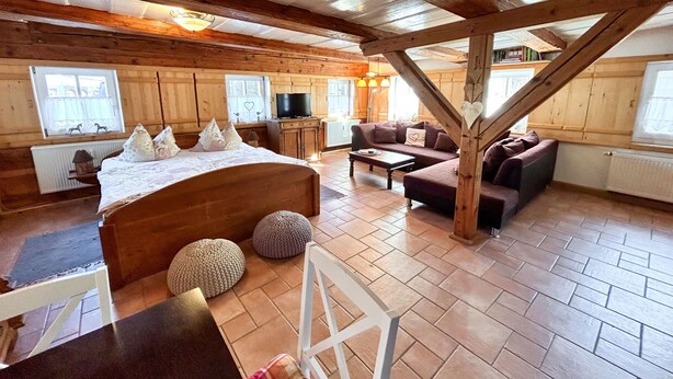 A cozy log cabin interior with a wooden bed, sofa, and dining area, featuring a television and large windows. - Vacation home Selma by Interhome (Grossschönau)