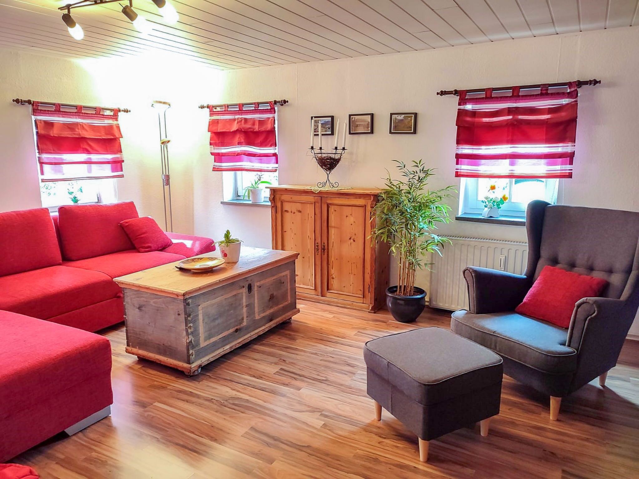 A cozy living room with a red sofa, a wooden coffee table, a grey armchair, and a potted plant.