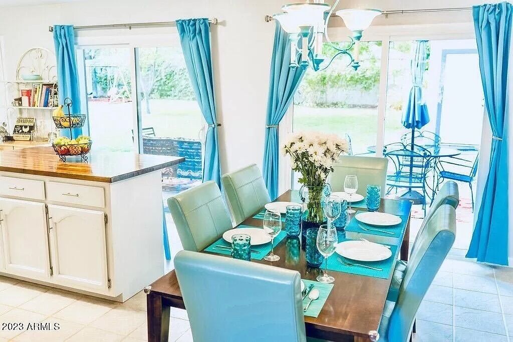 A dining area with a table set for four, blue curtains, and a view of the outdoors.
