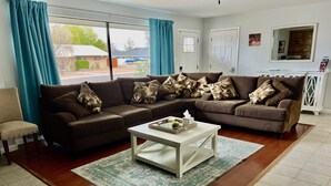 Ein Wohnzimmer mit einem braunen Ecksofa, einem weißen Couchtisch und Blick ins Freie durch große Fenster.