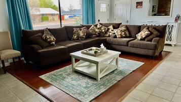 A living room with a brown sectional sofa, a white coffee table, and a view of the outside through large windows.