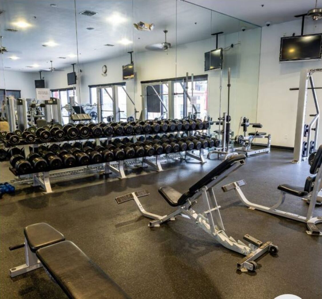 Un gimnasio con equipo de levantamiento de pesas, mancuernas y máquinas de ejercicio.