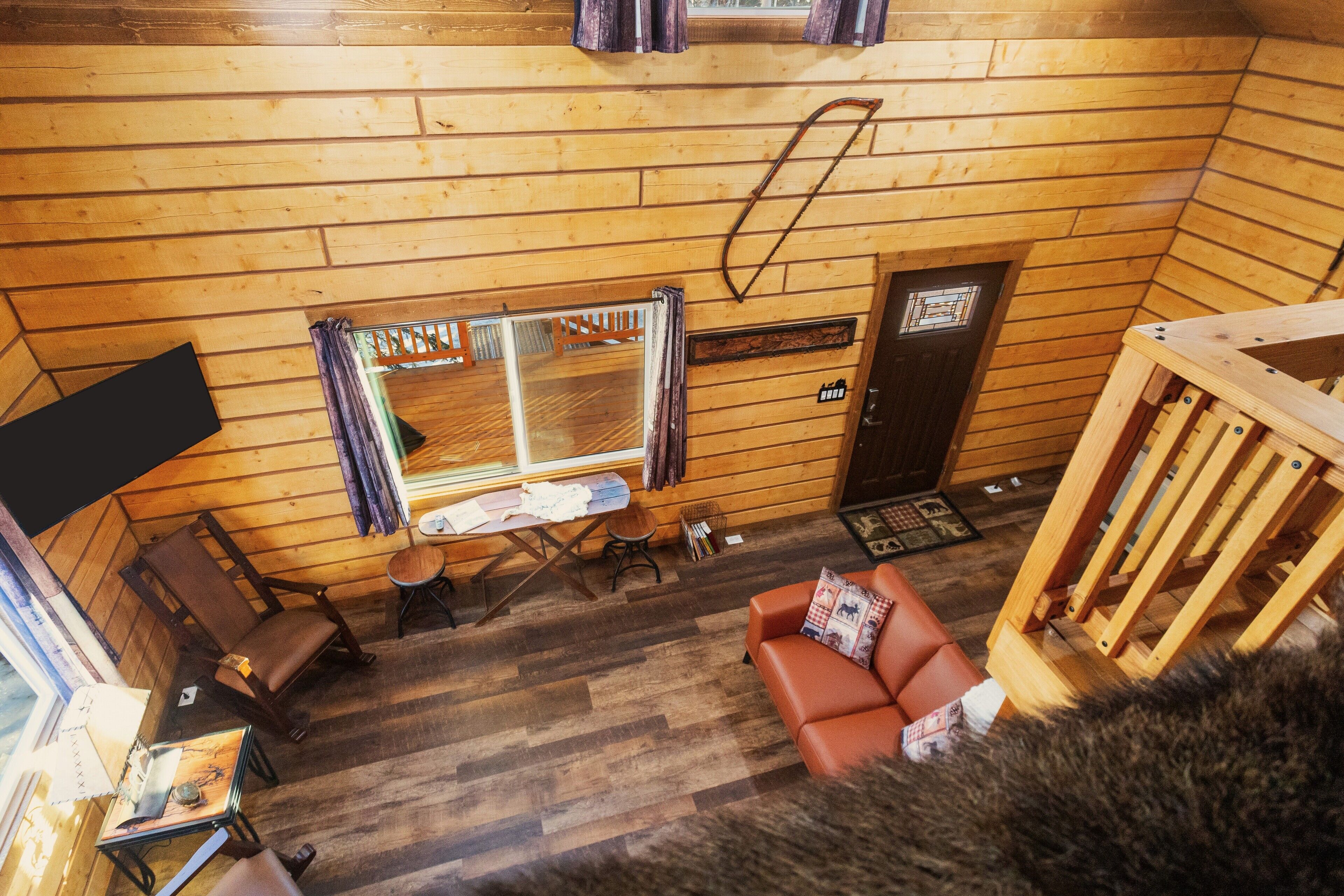 A cozy cabin interior with wooden walls, a sofa, a table, and a window.