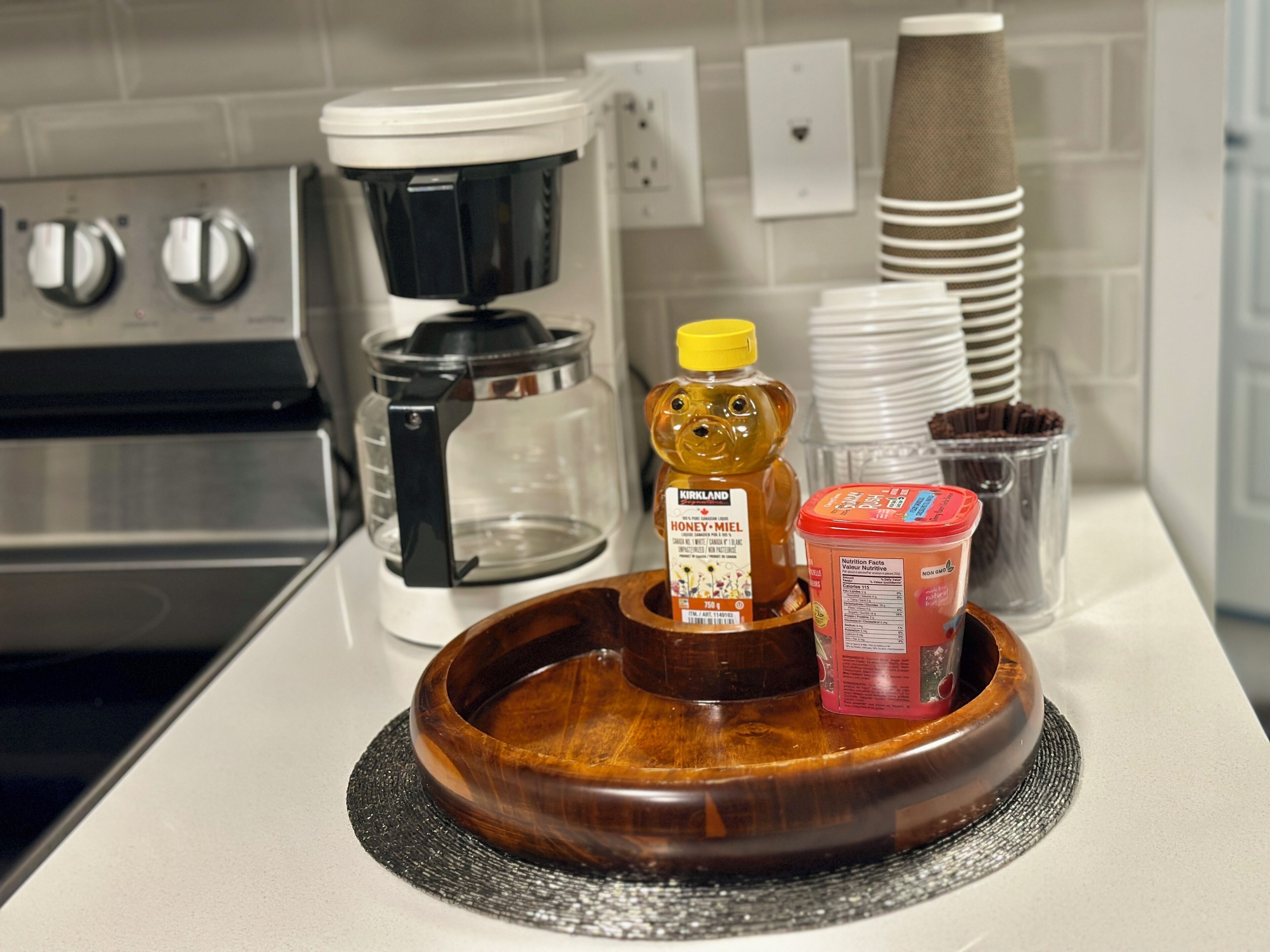 A kitchen counter with a coffee maker, a honey jar, a bear-shaped honey dipper, and a jar of peanut butter.
